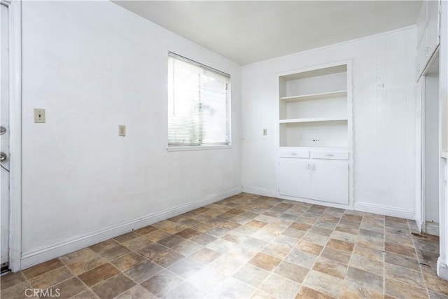 spare room with stone finish flooring, built in shelves, and baseboards