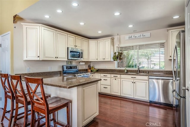 kitchen with recessed lighting, appliances with stainless steel finishes, dark wood-type flooring, a sink, and a peninsula