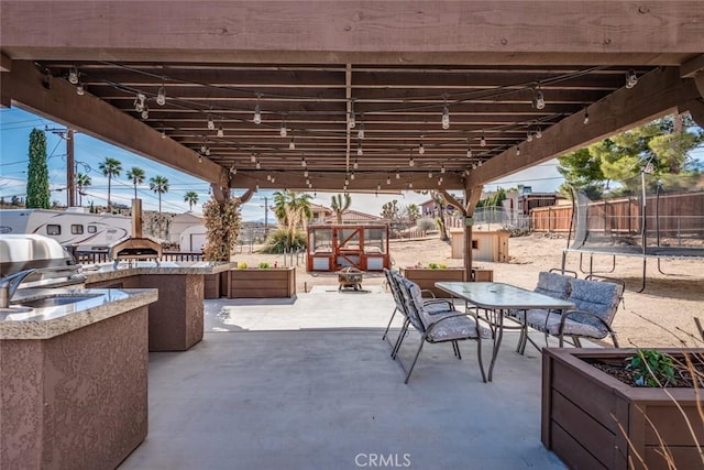 view of patio / terrace with a trampoline, outdoor dining area, area for grilling, and fence