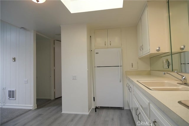 kitchen featuring light wood finished floors, visible vents, freestanding refrigerator, light countertops, and a sink