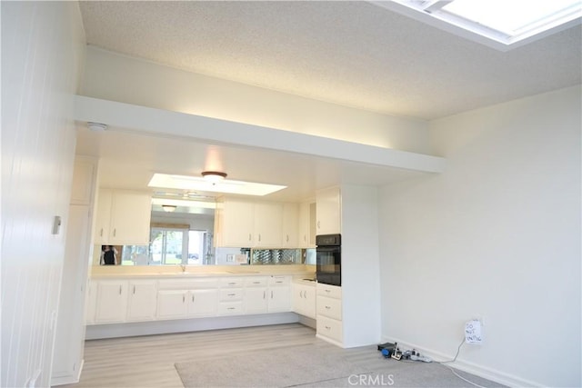 kitchen featuring light countertops, a skylight, black oven, and white cabinetry