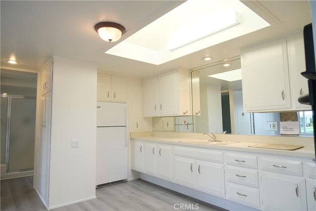 kitchen featuring freestanding refrigerator, light countertops, a sink, and white cabinetry