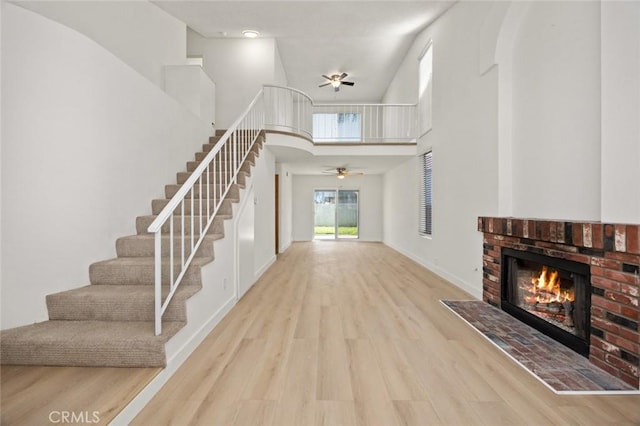 entrance foyer with a ceiling fan, a towering ceiling, wood finished floors, stairs, and a fireplace