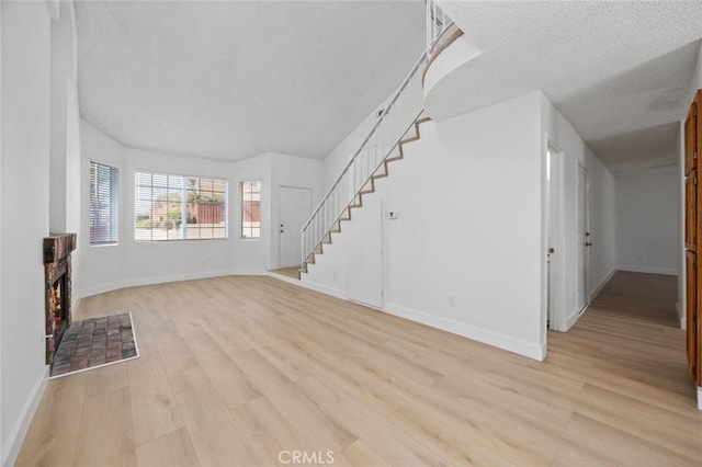 unfurnished living room featuring a textured ceiling, a fireplace, baseboards, stairway, and light wood-type flooring