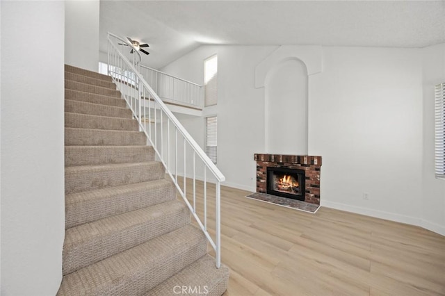 staircase with high vaulted ceiling, a fireplace, baseboards, and wood finished floors