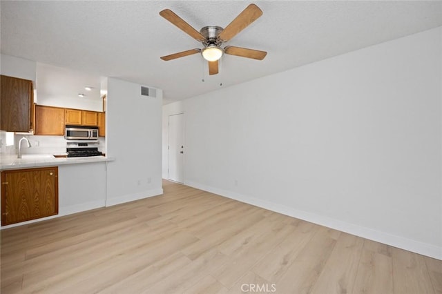 kitchen featuring brown cabinetry, gas range, stainless steel microwave, light countertops, and a sink