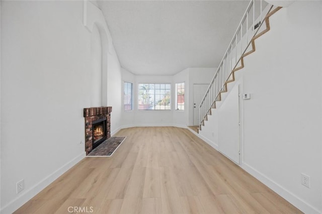 unfurnished living room with light wood-type flooring, a brick fireplace, baseboards, and stairway