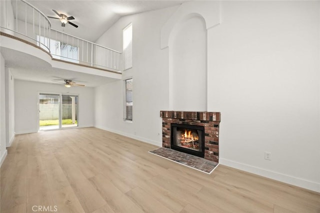 unfurnished living room with a fireplace, ceiling fan, wood finished floors, high vaulted ceiling, and baseboards