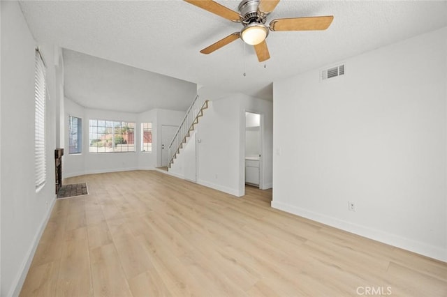 unfurnished living room featuring visible vents, light wood-style flooring, a textured ceiling, and stairs