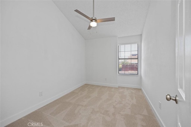 empty room with ceiling fan, a textured ceiling, light carpet, baseboards, and vaulted ceiling