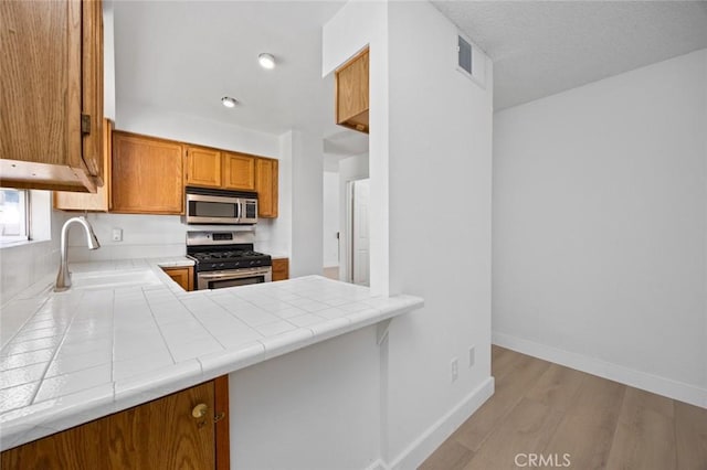 kitchen with brown cabinets, tile countertops, appliances with stainless steel finishes, a sink, and baseboards