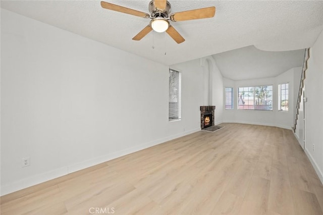 unfurnished living room with a textured ceiling, ceiling fan, a warm lit fireplace, baseboards, and light wood finished floors