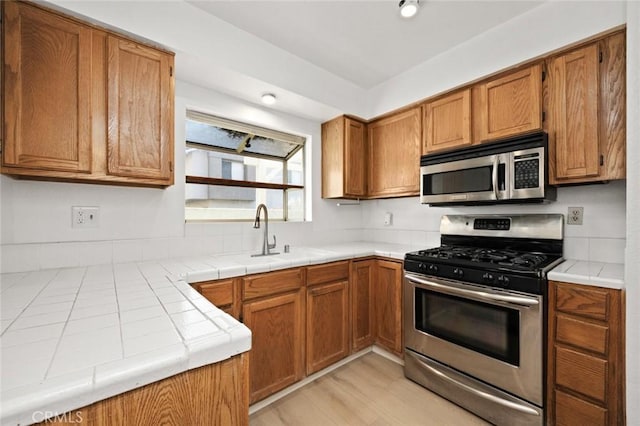 kitchen featuring appliances with stainless steel finishes, a sink, tile counters, and brown cabinets