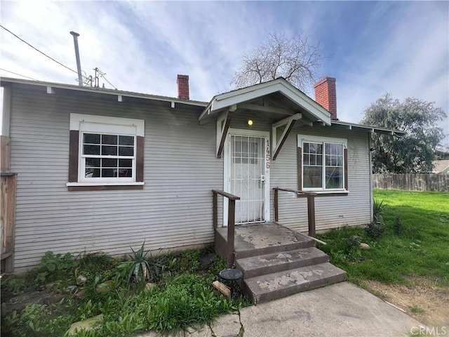 bungalow-style home featuring a front lawn, a chimney, and fence