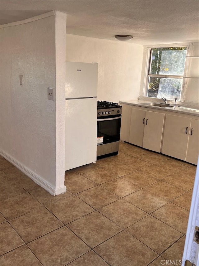 kitchen featuring freestanding refrigerator, gas stove, white cabinets, a sink, and tile patterned floors