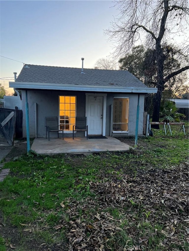 rear view of property with roof with shingles, fence, a lawn, and a patio