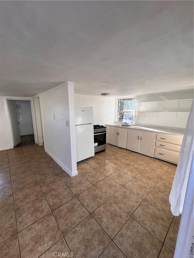 kitchen with stainless steel range with gas cooktop, freestanding refrigerator, a textured ceiling, and light tile patterned floors