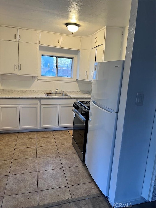 kitchen with light tile patterned floors, freestanding refrigerator, black range with gas stovetop, white cabinetry, and a sink