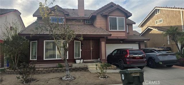 view of front facade featuring a tiled roof, concrete driveway, a chimney, and an attached garage