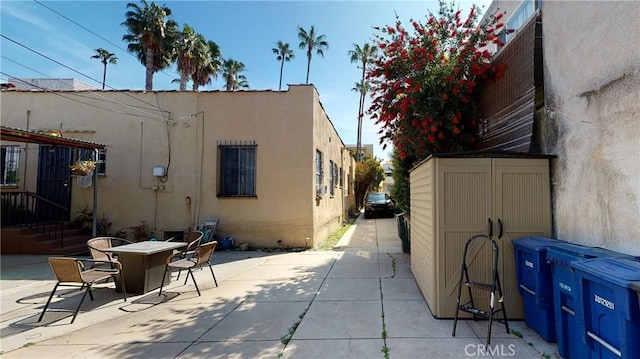 view of side of property featuring a storage shed, stucco siding, an outbuilding, a patio area, and outdoor dining space