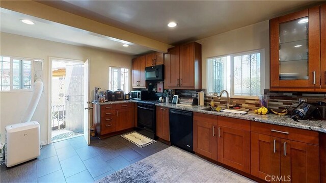 kitchen featuring tasteful backsplash, glass insert cabinets, a sink, light stone countertops, and black appliances