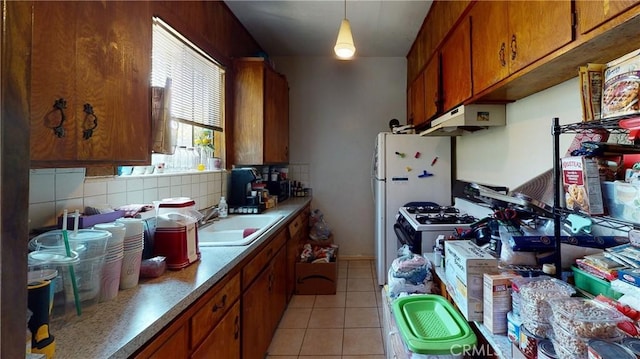 kitchen with white appliances, light tile patterned floors, brown cabinets, under cabinet range hood, and a sink