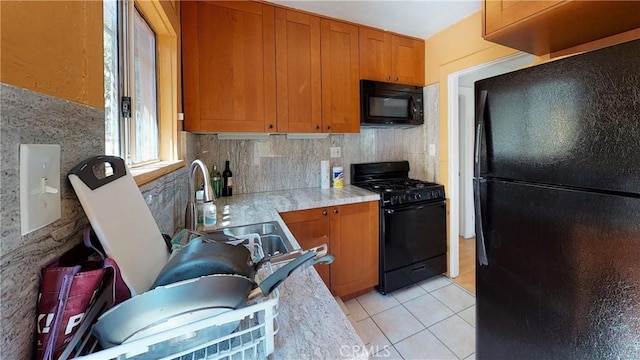 kitchen with light tile patterned floors, brown cabinets, light countertops, black appliances, and a sink