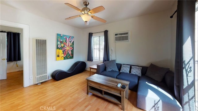 living room featuring ceiling fan, light wood-type flooring, a wall unit AC, and a heating unit