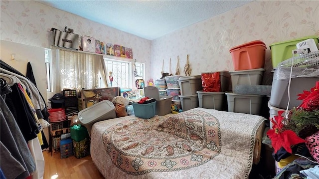 bedroom featuring wood finished floors, a textured ceiling, and wallpapered walls