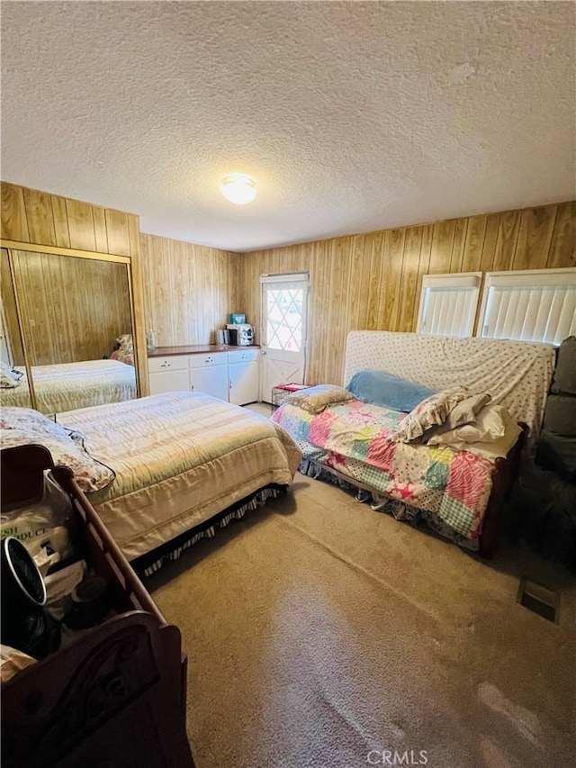 bedroom featuring carpet floors, wood walls, visible vents, and a textured ceiling