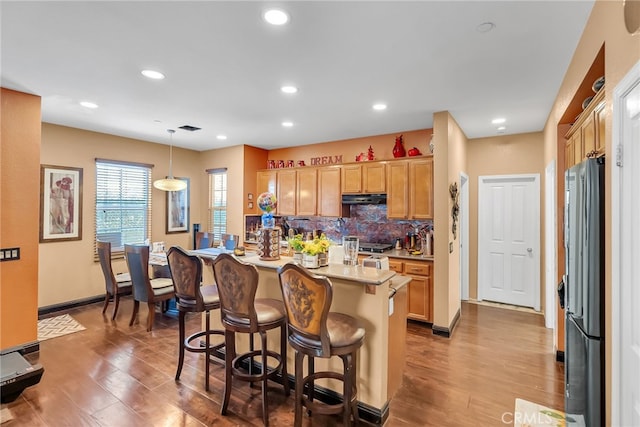 kitchen featuring decorative backsplash, wood finished floors, freestanding refrigerator, light countertops, and under cabinet range hood