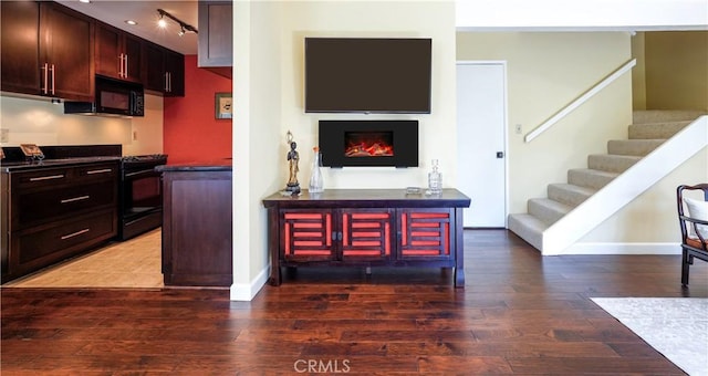 kitchen featuring dark countertops, hardwood / wood-style floors, a lit fireplace, black appliances, and track lighting