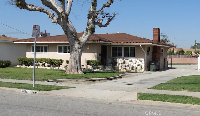 ranch-style home with driveway, a chimney, a tiled roof, a front yard, and stucco siding