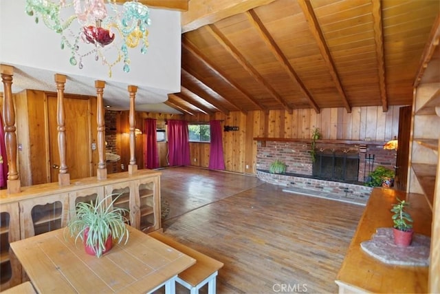 unfurnished dining area with lofted ceiling with beams, a brick fireplace, wood walls, wood finished floors, and wooden ceiling