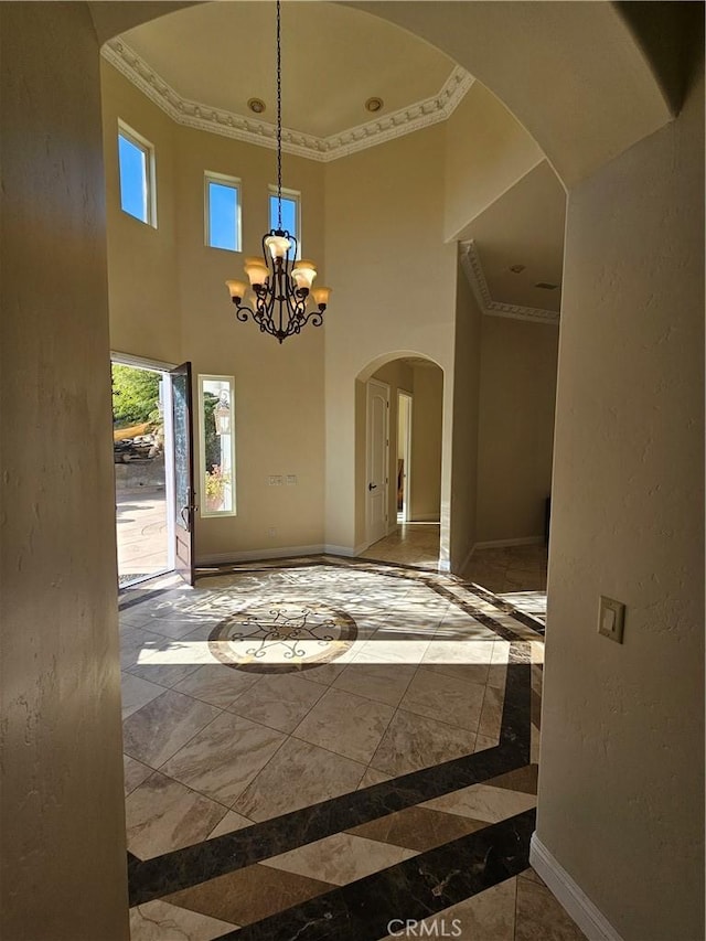 interior space with arched walkways, a textured wall, a chandelier, baseboards, and ornamental molding