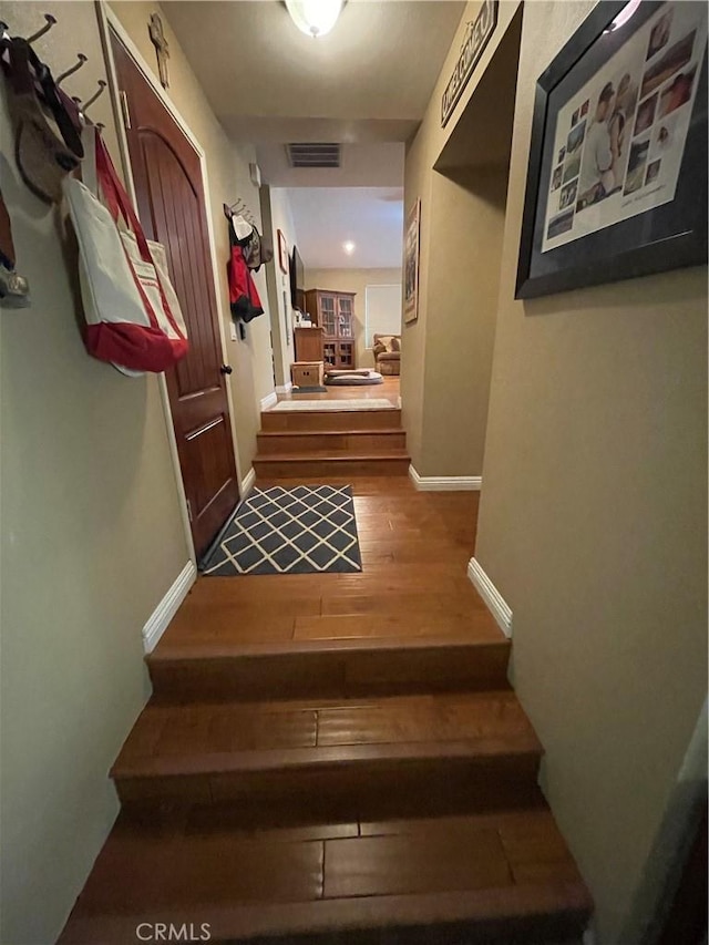 corridor with visible vents, baseboards, wood finished floors, and stairs