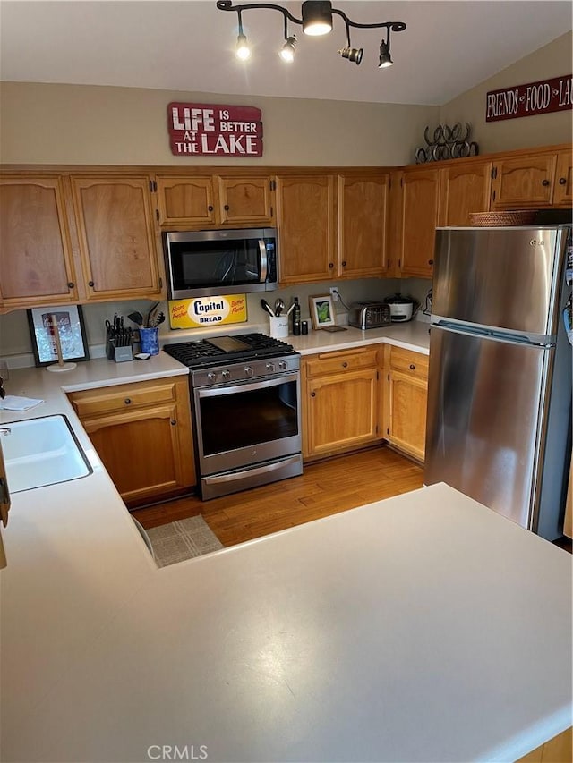 kitchen with light wood-type flooring, a sink, appliances with stainless steel finishes, light countertops, and lofted ceiling