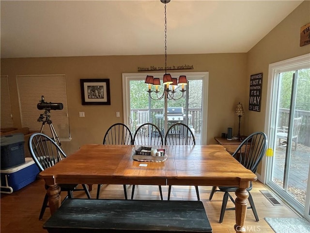 dining space featuring vaulted ceiling, a notable chandelier, visible vents, and light wood finished floors