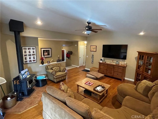 living room with baseboards, ceiling fan, a wood stove, and light wood finished floors