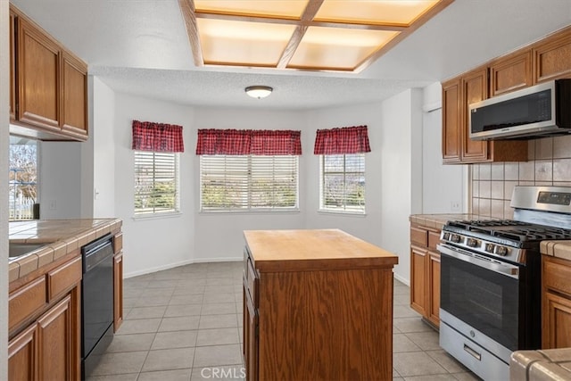 kitchen with a center island, tile counters, backsplash, appliances with stainless steel finishes, and light tile patterned flooring