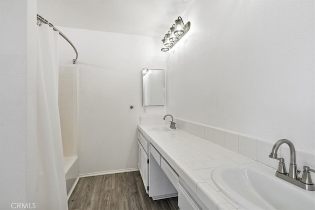 bathroom with double vanity, baseboards, a sink, and wood finished floors