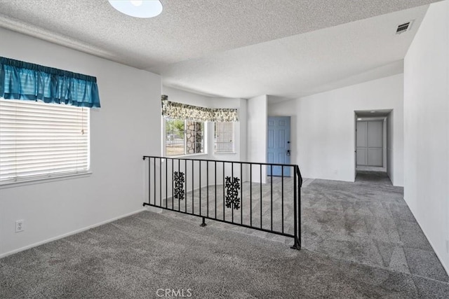 empty room with carpet floors, visible vents, vaulted ceiling, and a textured ceiling