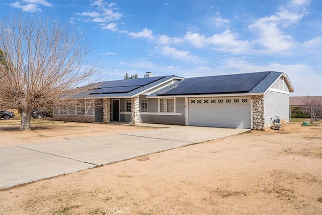 ranch-style house with a garage, solar panels, stone siding, driveway, and a chimney