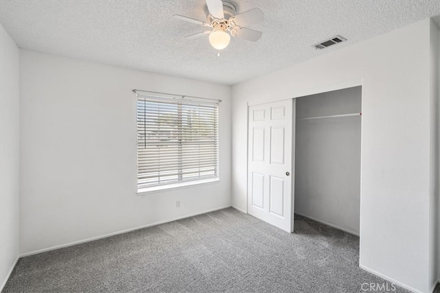 unfurnished bedroom with a textured ceiling, ceiling fan, carpet flooring, visible vents, and a closet