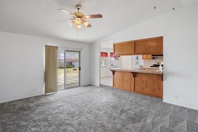 kitchen featuring carpet floors, brown cabinets, tile countertops, vaulted ceiling, and ventilation hood