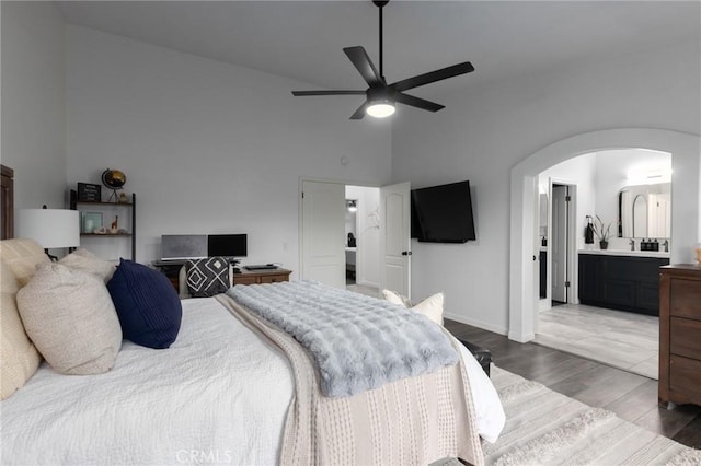 bedroom featuring arched walkways, a ceiling fan, connected bathroom, dark wood-type flooring, and a high ceiling