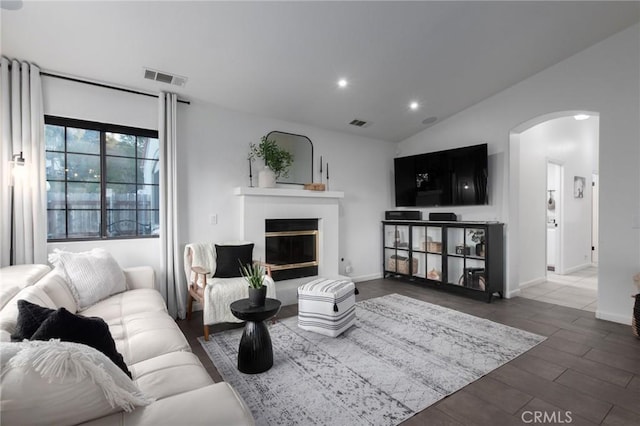 living room featuring arched walkways, vaulted ceiling, a glass covered fireplace, and visible vents