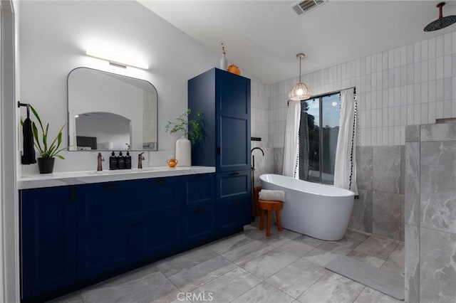 full bath featuring visible vents, vanity, vaulted ceiling, a freestanding bath, and tile walls