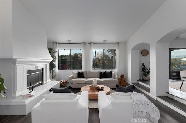 living room featuring a glass covered fireplace, dark wood-style flooring, visible vents, and arched walkways