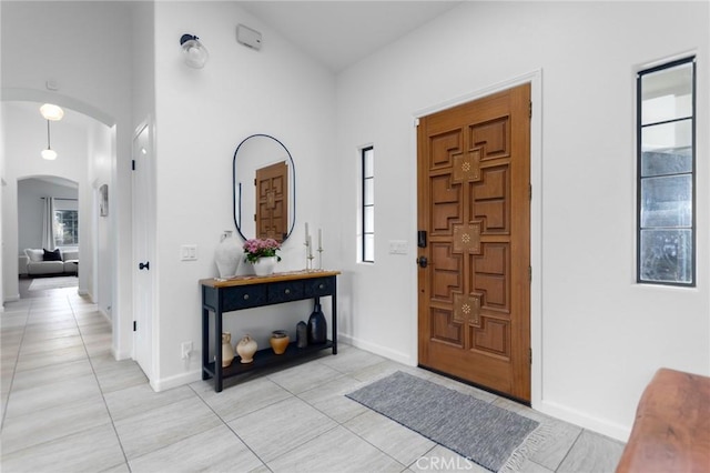 foyer featuring arched walkways, light tile patterned floors, a towering ceiling, and baseboards